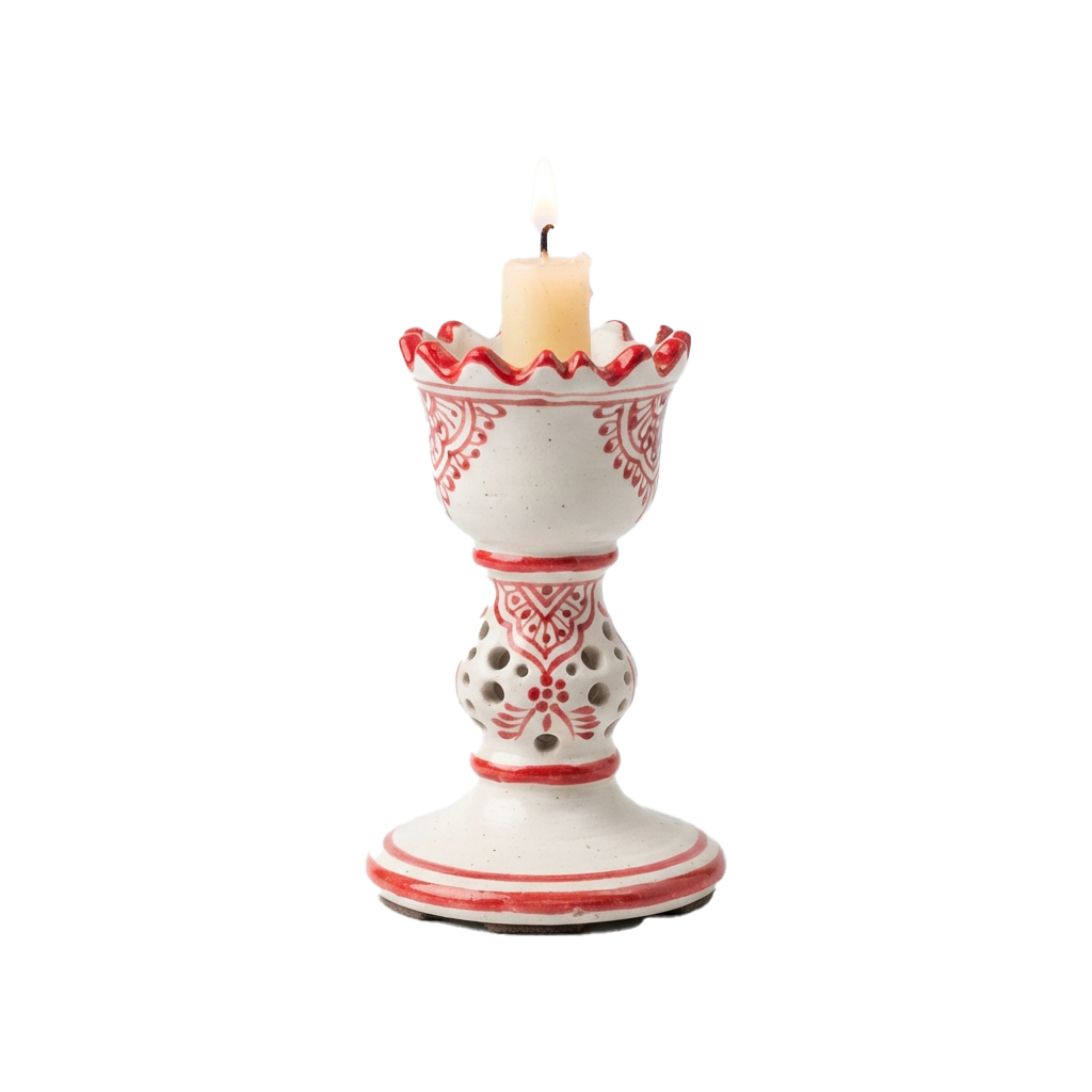A white candle with red floral patterns and scalloped edges burning inside a matching decorative holder