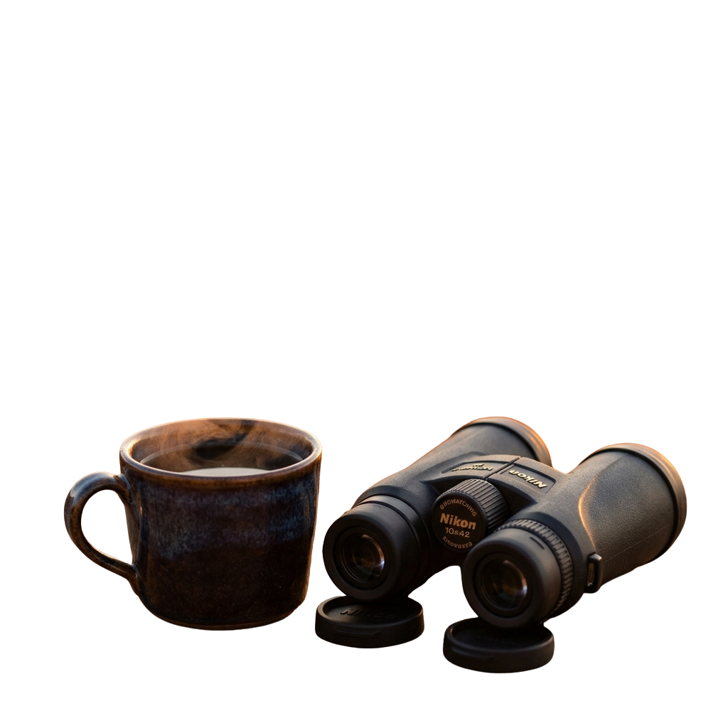A ceramic mug filled with liquid and a pair of binoculars on a dark background