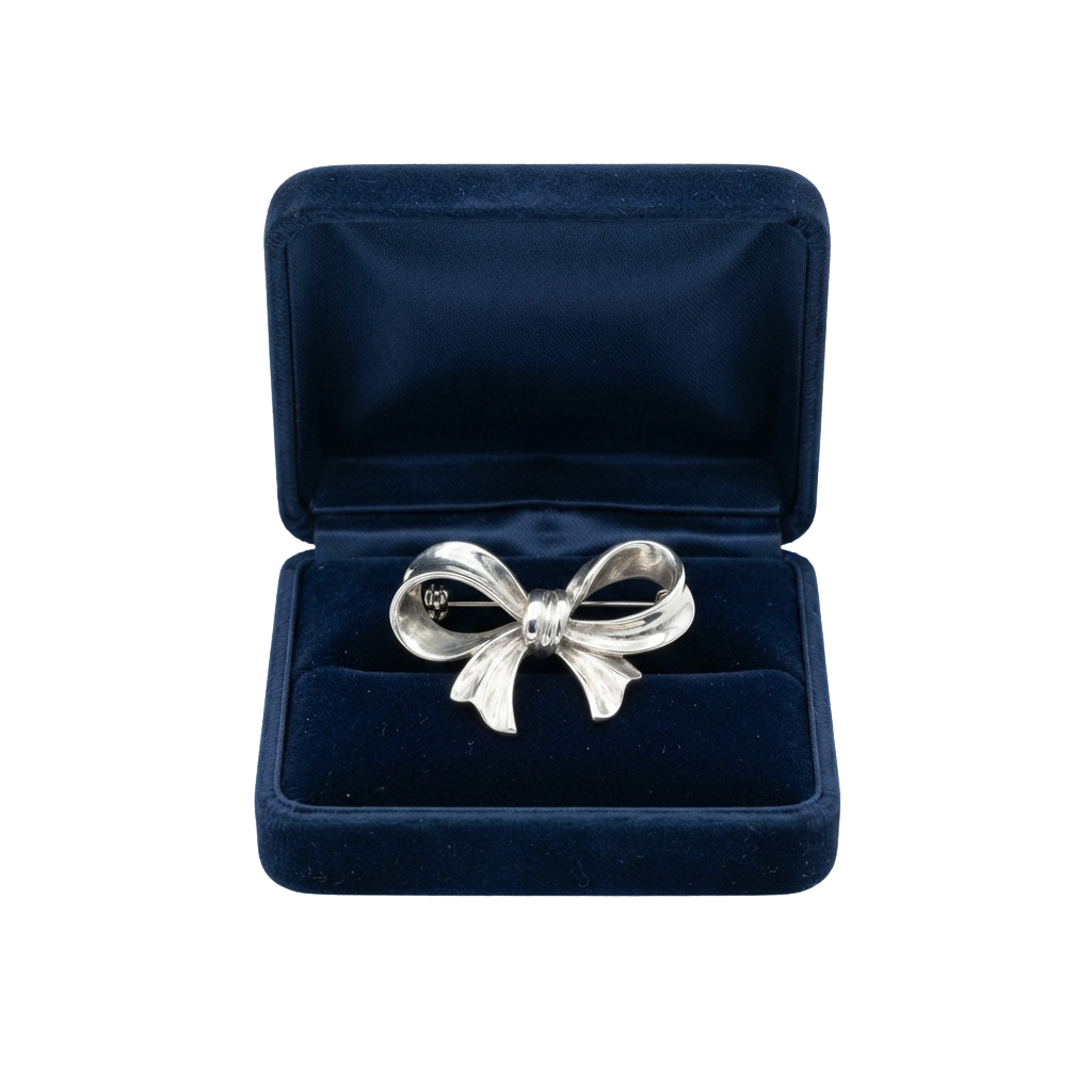 A silver bow-shaped brooch displayed inside a dark velvet jewelry box