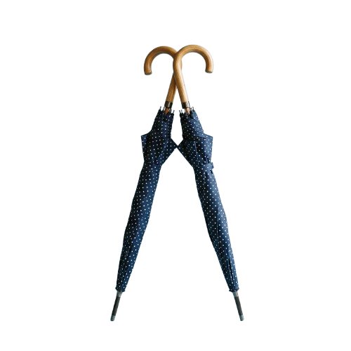 Blue umbrella with white polka dots and a wooden handle standing upright against a dark background