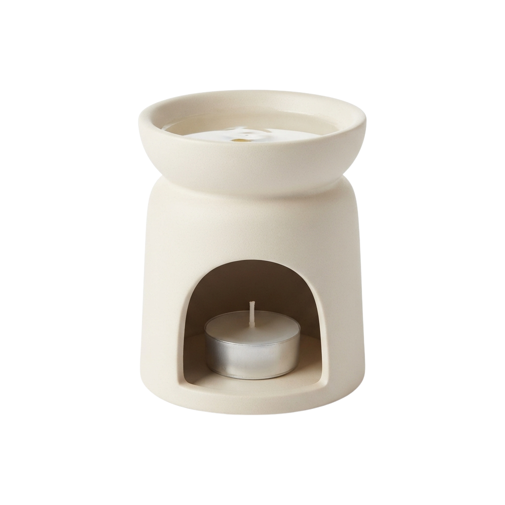 A white ceramic tea light warmer with a candle inside an arched opening at the front and a lid on top