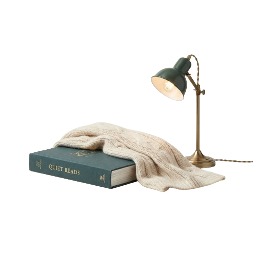 A book titled Quiet Reads covered with a light-colored knit blanket and a small desk lamp turned on beside it