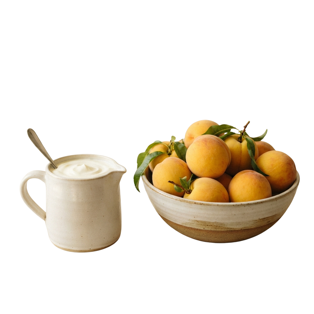 A ceramic pitcher filled with cream and a bowl of fresh peaches with green leaves