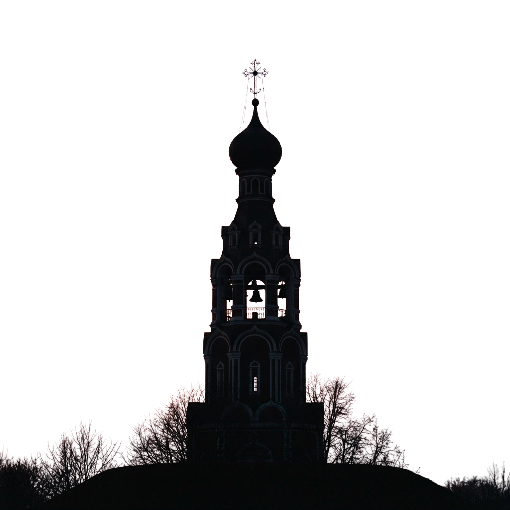Silhouette of an illuminated Orthodox church tower with a cross at night, surrounded by dark trees.