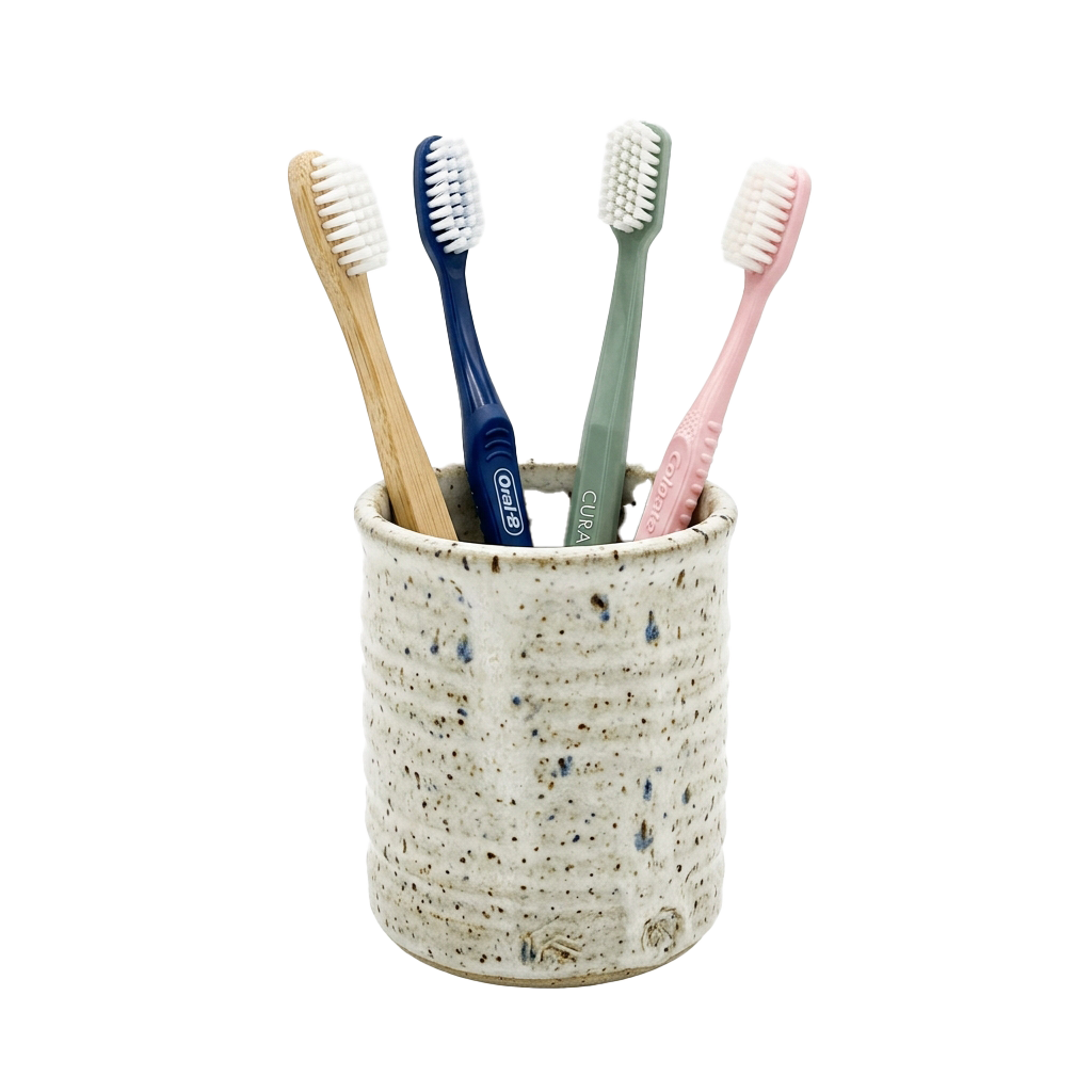 A ceramic toothbrush holder with four different colored toothbrushes standing upright inside it.
