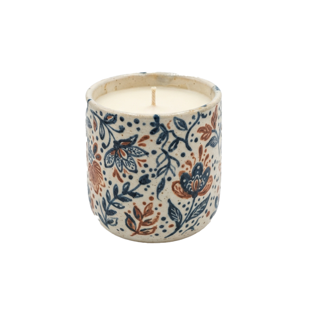 Ceramic candle with floral and leaf patterns in blue, orange, and white against a black background